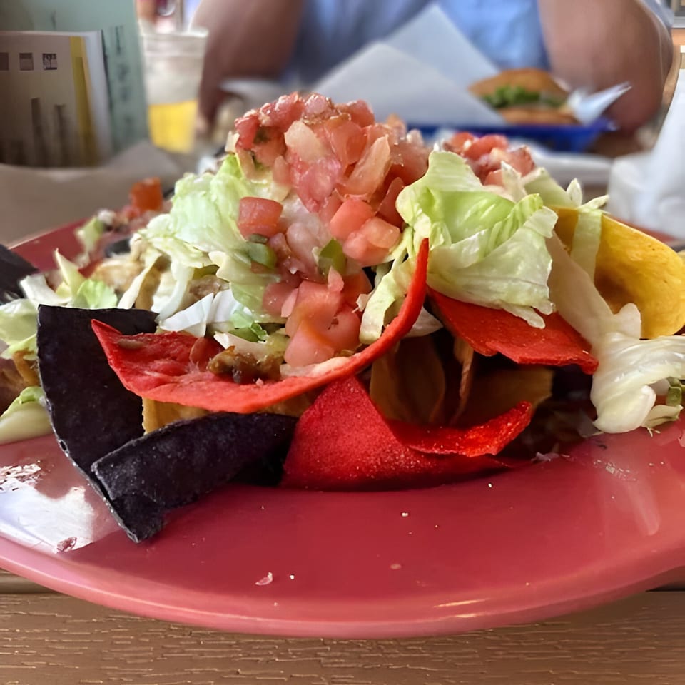 A vibrant plate of nachos with red, black, and yellow chips, topped with lettuce and diced tomatoes.