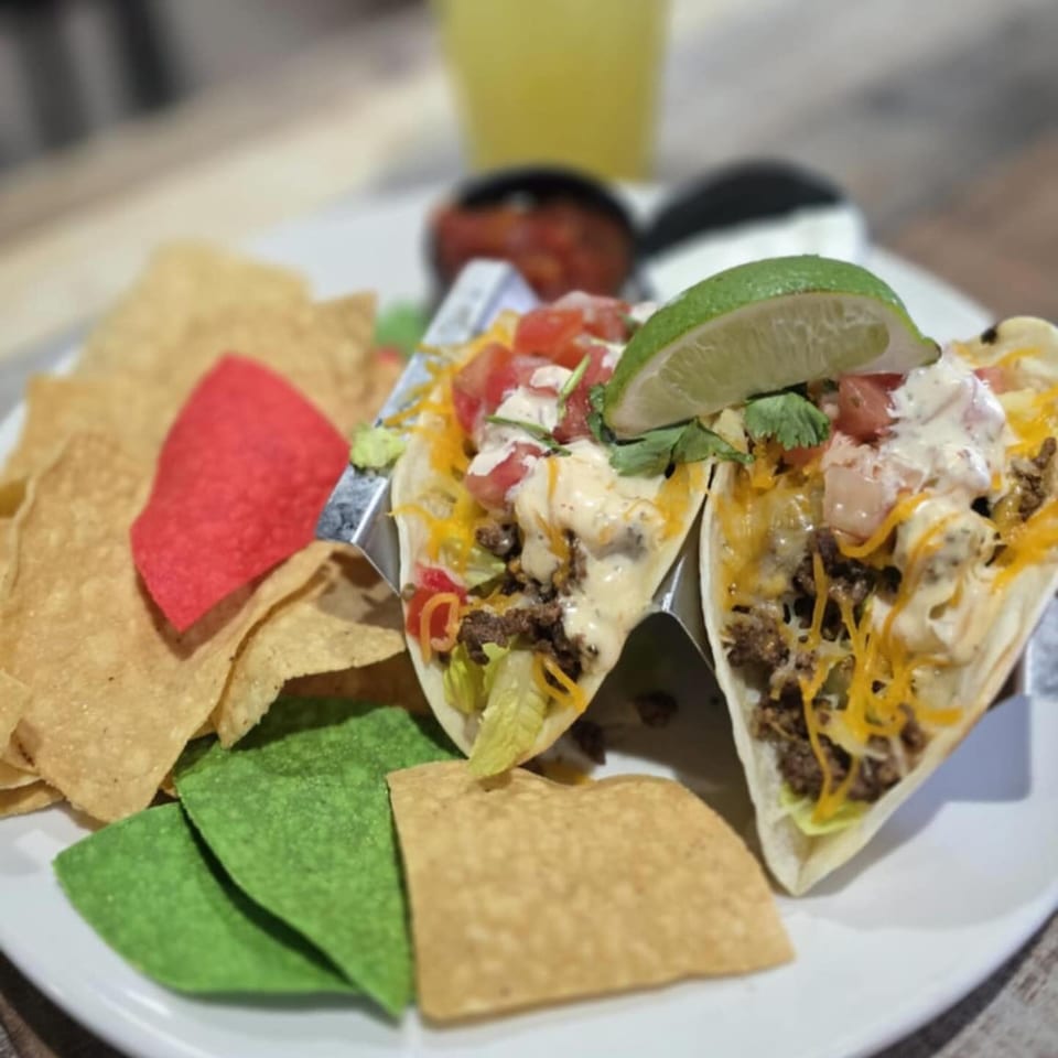 Two soft tacos with ground beef, cheese, lettuce, tomatoes, and sauce, served with tortilla chips.