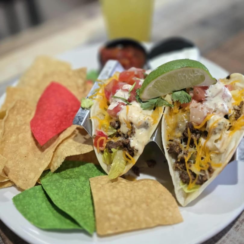 Two soft tacos with ground beef, cheese, lettuce, tomatoes, and sauce, served with tortilla chips.