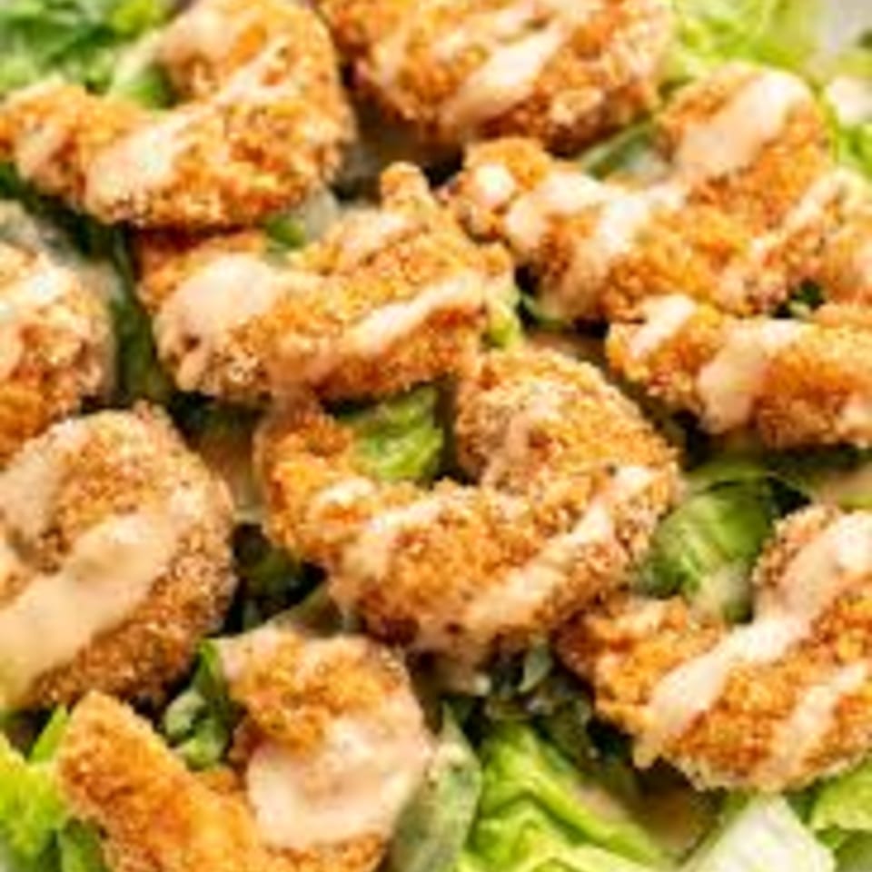 Crispy fried shrimp drizzled with sauce, served over a bed of fresh green lettuce.