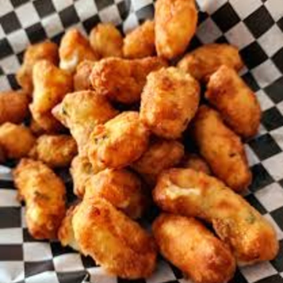 A close-up of golden-brown fried cheese curds in a black and white checkered paper liner.
