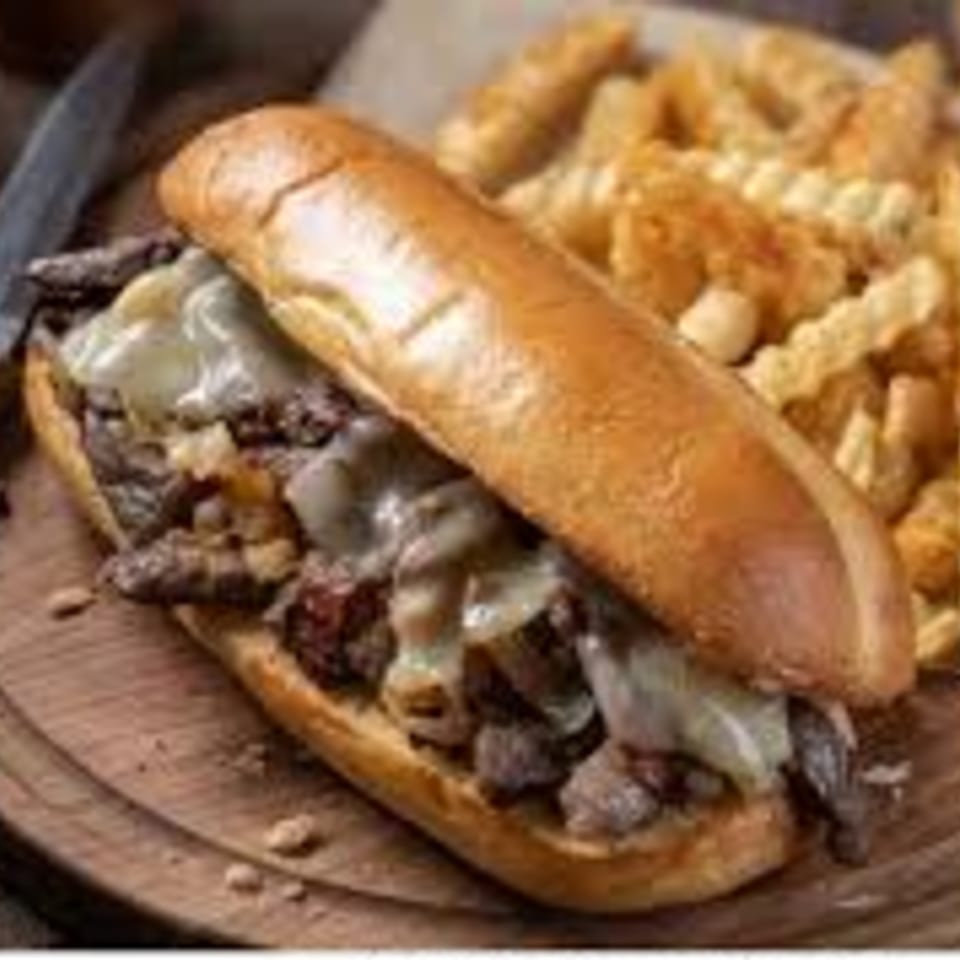Kings Roadhouse Bar & Grill's Philly cheesesteak sandwich with melted cheese, steak, and a side of fries.